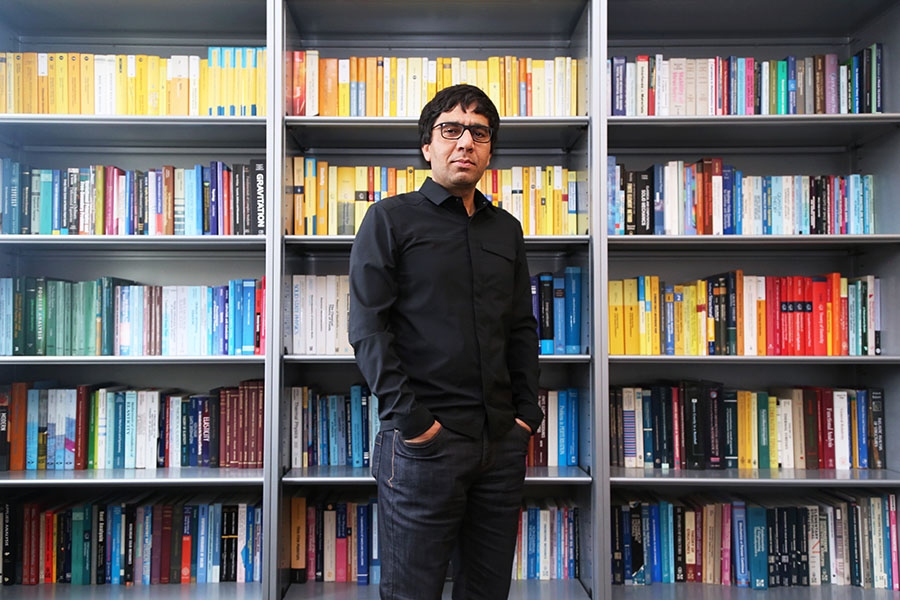 Professor Arash Yavari stands in front of his packed bookcase in his Mason Building office. Yavari has embarked upon a four-year research project to lay the mathematical foundations for cloaking structures from earthquakes and other stress waves. (Photo: Jess Hunt-Ralston)